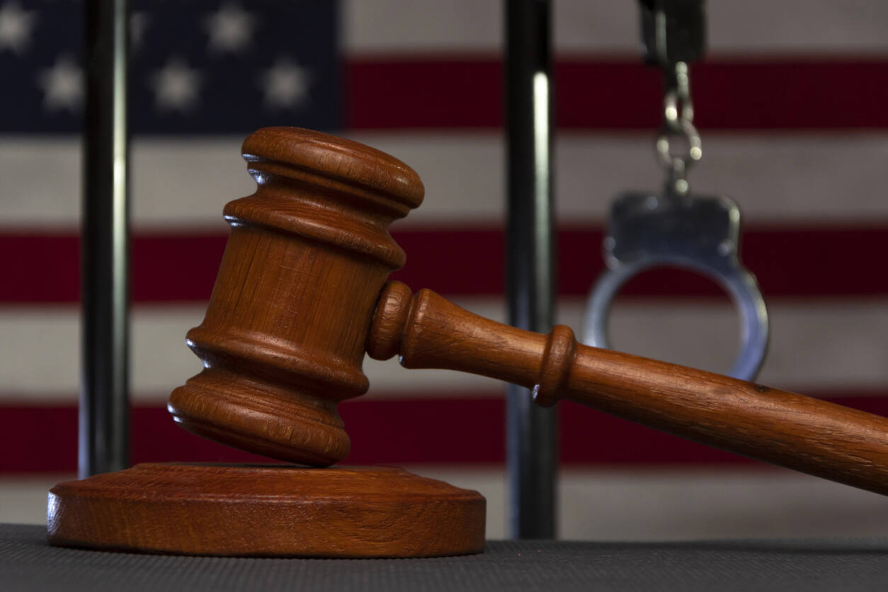 A judge's gavel lies in the foreground with handcuffs and an American flag visible through prison bars in the background, symbolizing how a criminal conviction can profoundly affect an individual's future and freedom.
