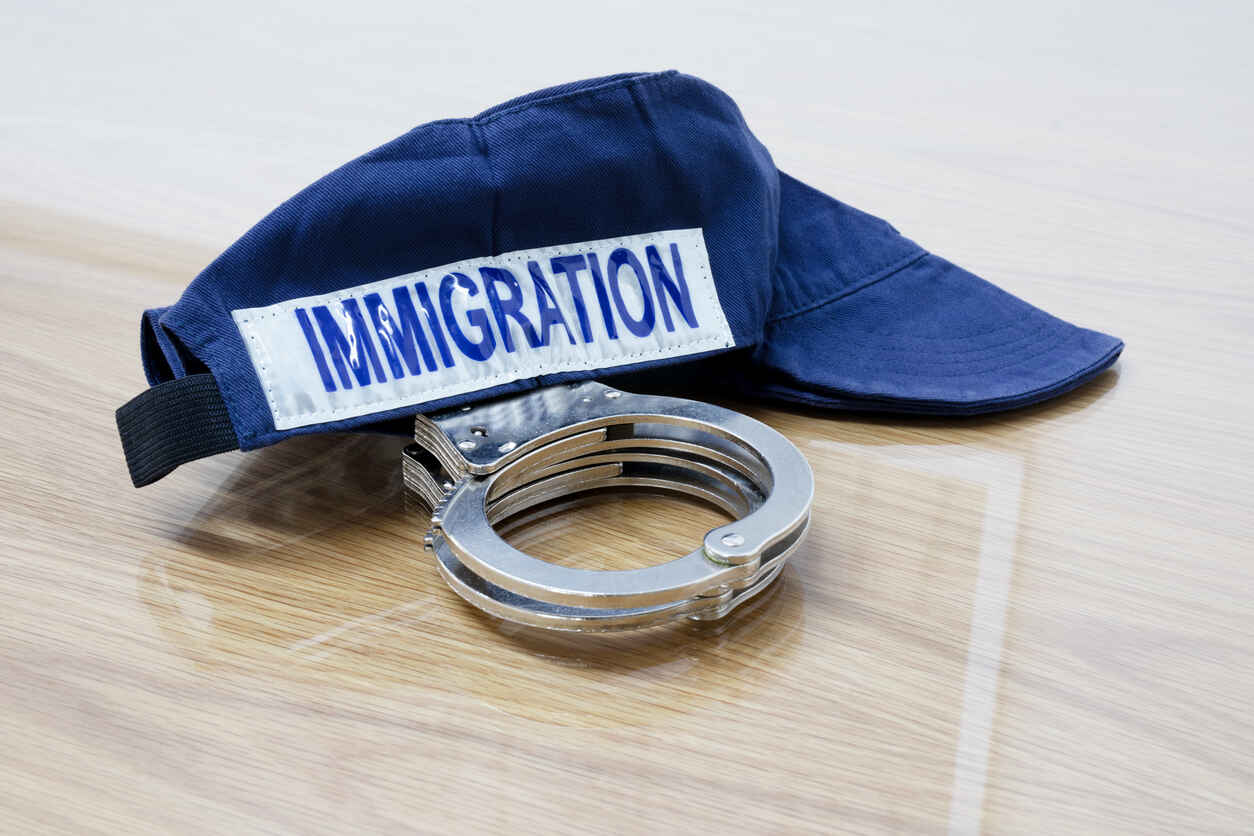 A blue cap with 'IMMIGRATION' written on it lies next to a pair of handcuffs, symbolizing the expanded local role in federal immigration enforcement under a new law.