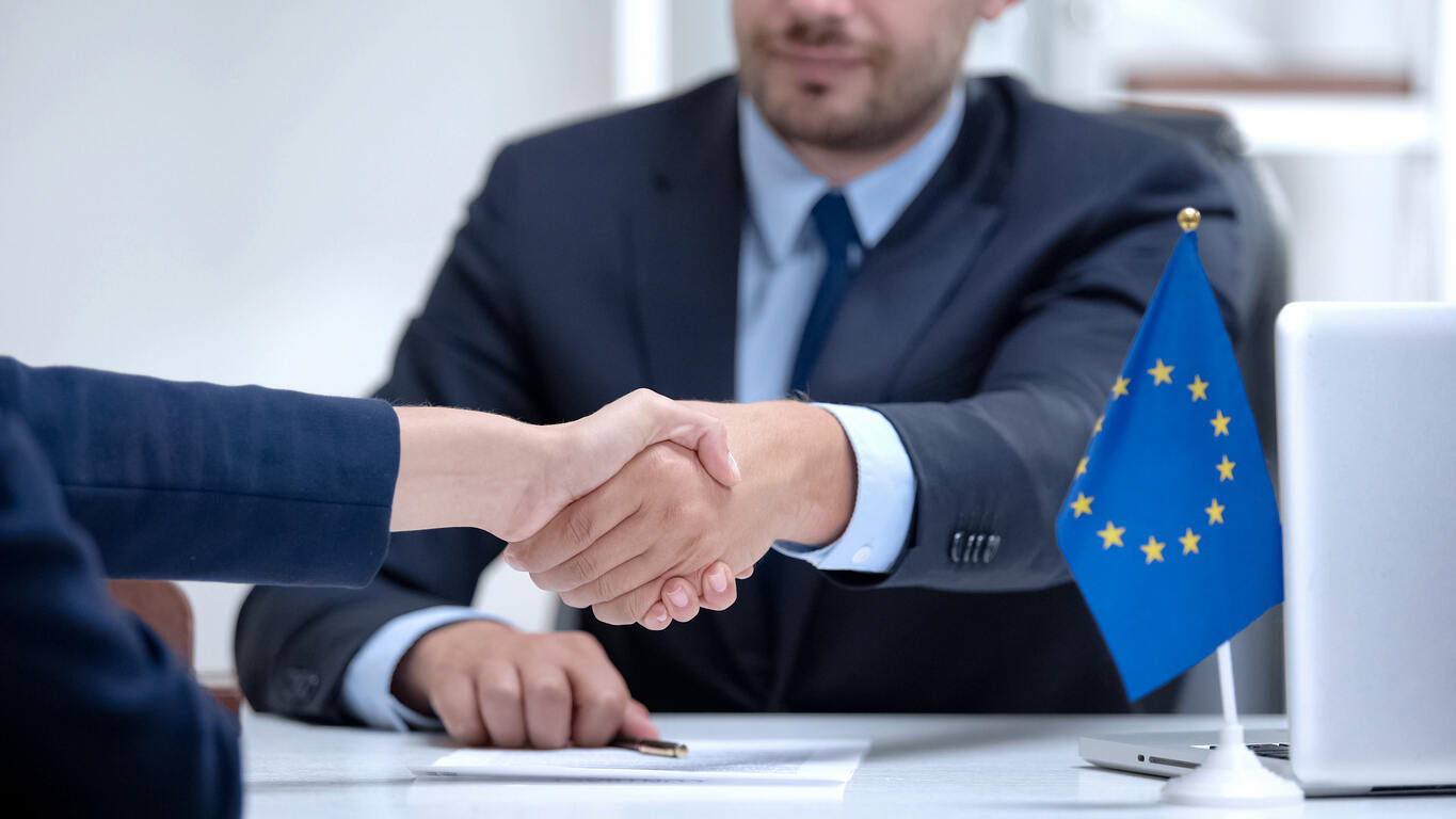  Businessman shaking hands with a European flag, symbolizing international trade and E-1 Treaty Trader Visa inquiries in Austin. 